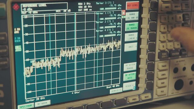 hand held close up shot of spectrum analyzer screen with megahertz decibels and other readings, finger push buttons