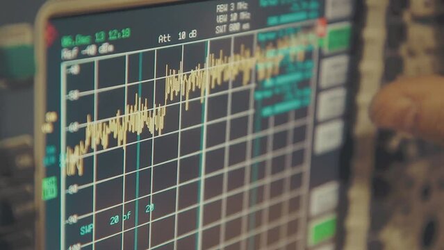 hand held close up shot of spectrum analyzer screen with megahertz decibels and other readings, finger push buttons