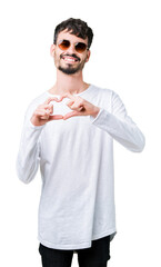 Young handsome man wearing sunglasses over isolated background smiling in love showing heart symbol and shape with hands. Romantic concept.