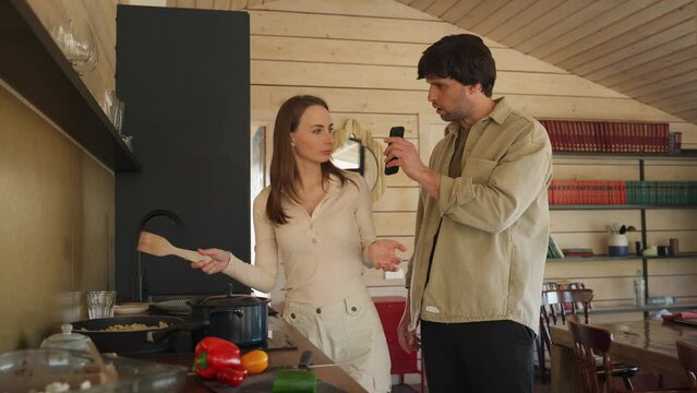Infidelity. A jealous husband shows his cheating wife her phone, demanding an explanation, standing in the kitchen. Husband caught his wife cheating with a mobile phone - divorcing people. 