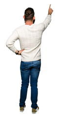 Young hipster man wearing winter sweater Posing backwards pointing behind with finger hand
