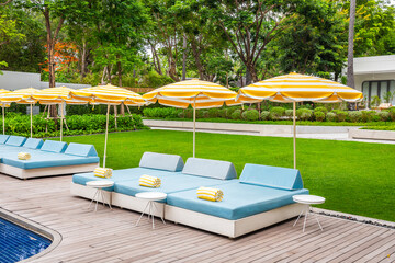 Pool chairs with umbrellas and beautiful water reflections by the sea with green grass in the background.