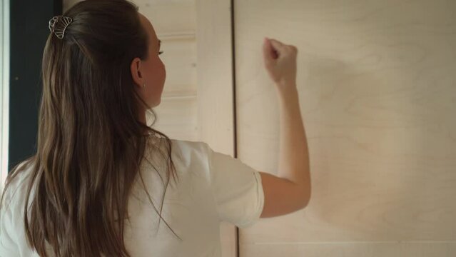 Woman knocks on a wooden door, standing in the doorway. Rear view of a woman knocking on the door. A visitor wants to enter the house.