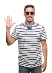 Naklejka premium Handsome young man wearing headphones showing and pointing up with fingers number five while smiling confident and happy.