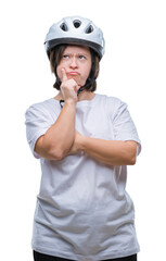 Young adult cyclist woman with down syndrome wearing safety helmet over isolated background with hand on chin thinking about question, pensive expression. Smiling with thoughtful face. Doubt concept.