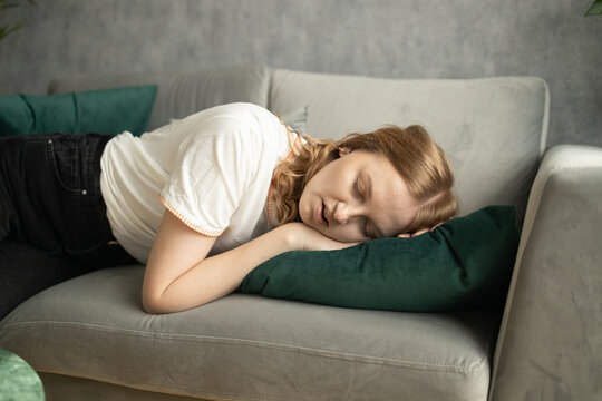 Peaceful young 30s woman lying barefooted on the sofa and closing her eyes while falling asleep with one hand touching the floor. High quality photo