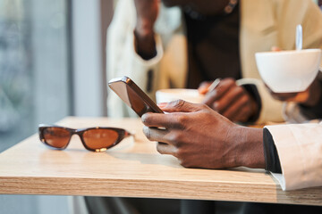 Cropped view of multiracial male people sitting at the cafeteria table and using smartphone