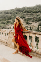Woman red dress. Summer lifestyle of a happy woman posing near a fence with balusters over the sea.