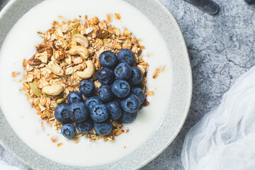 Granola with yogurt and blueberries in a plate on a gray background