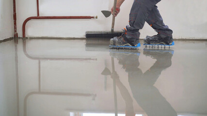 A worker uses epoxy concrete screed to level. Leveling with cement mix for floors. Pours a liquid...