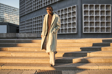 Full length view of multiracial man in casual style trench coat standing at street stairs