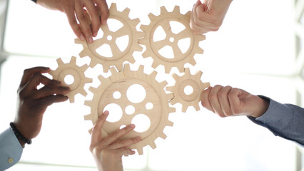 Hands holding a wooden gear by businessmen for workplace harmony in the office. bottom view