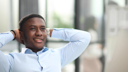 Young businessman sitting in office with hands behind his head satisfied with work done