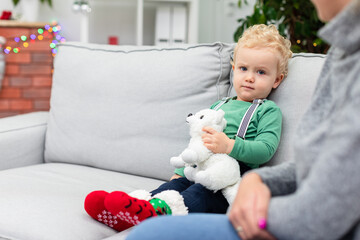 A young child sits on the couch and plays with a teddy bear