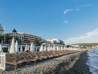 Nice, France - July 10, 2023: Evening on the beach of Nice, empty sun loungers at the setting sun and closed sun umbrellas