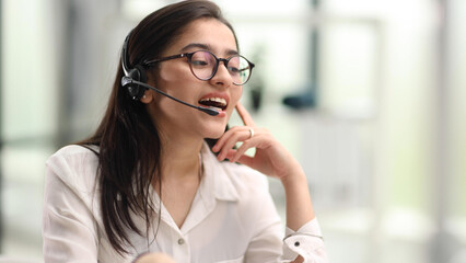 Portrait of a young woman in a headset working in an office center online from a laptop.