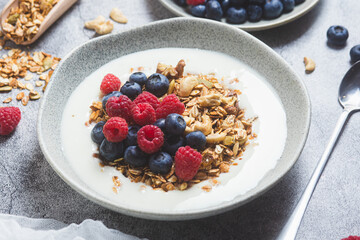 Granola with yogurt, raspberries, blueberries in a plate on a gray background