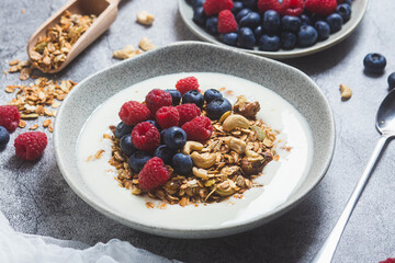 Granola with yogurt, raspberries, blueberries in a plate on a gray background