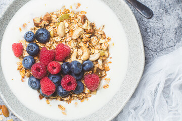 Granola with yogurt, raspberries, blueberries in a plate on a gray background