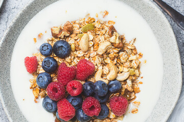 Granola with yogurt, raspberries, blueberries in a plate on a gray background