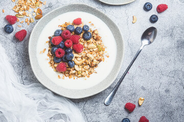 Granola with yogurt, raspberries, blueberries in a plate on a gray background