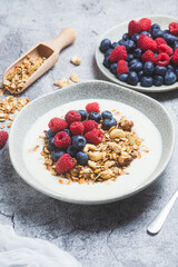 Granola with yogurt, raspberries, blueberries in a plate on a gray background