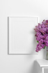 Blank portrait poster frame mockup on white wall with lilac flowers bouquet