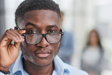 a black man in a blue shirt adjusts his glasses.