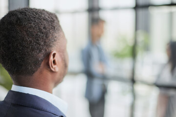 portrait of a black guy stands with his back and looks at his colleagues in the office