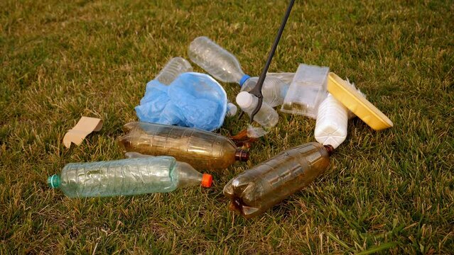 Close-up of a garbage collection tongs with a plastic bottle in the city. The concept of garbage collection and environmental protection. A volunteer collects plastic garbage.