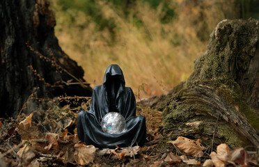black cloaked figure with crystal ball in mysterious autumn forest, natural background. esoteric...