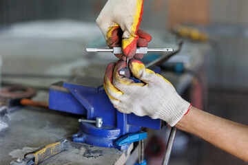 Threading with a die, a rasp, a metal spare part is clamped in vice on a workbench in workshop