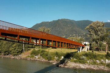 Modern rusted pedestrian and bicycle bridge with flowing Ticino river below. Beautiful panorama of...