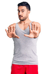 Young handsome man wearing swimwear and sleeveless t-shirt doing stop gesture with hands palms, angry and frustration expression