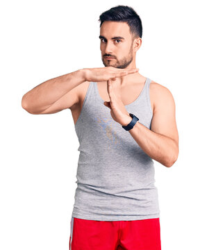 Young handsome man wearing swimwear and sleeveless t-shirt doing time out gesture with hands, frustrated and serious face