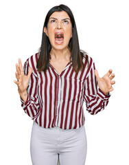 Beautiful brunette woman wearing striped shirt crazy and mad shouting and yelling with aggressive expression and arms raised. frustration concept.