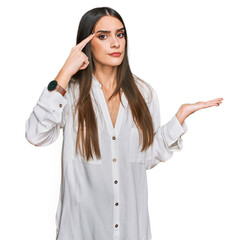 Young beautiful woman wearing casual white shirt confused and annoyed with open palm showing copy space and pointing finger to forehead. think about it.