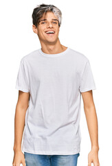 Fototapeta premium Young hispanic man wearing casual white tshirt looking positive and happy standing and smiling with a confident smile showing teeth