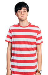 Handsome hipster young man wearing casual striped t shirt puffing cheeks with funny face. mouth inflated with air, crazy expression.