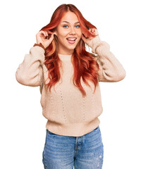 Young redhead woman wearing casual winter sweater smiling pulling ears with fingers, funny gesture. audition problem