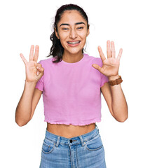 Hispanic teenager girl with dental braces wearing casual clothes showing and pointing up with fingers number eight while smiling confident and happy.