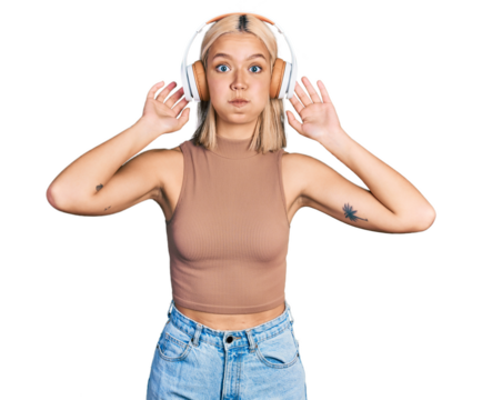 Beautiful young blonde woman listening to music using headphones puffing cheeks with funny face. mouth inflated with air, catching air. - Powered by Adobe
