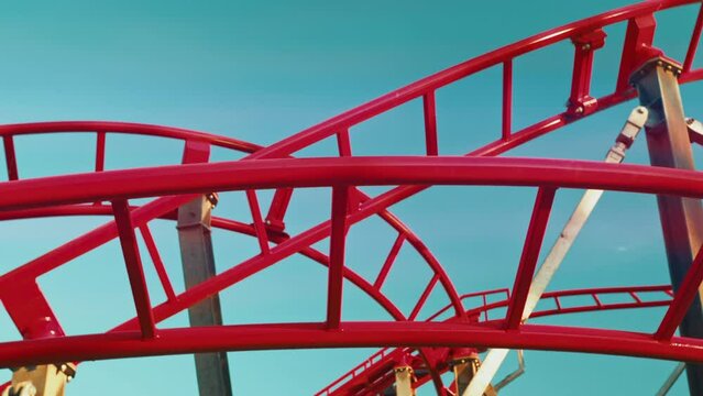 Close up bottom up view of twisting red roller coaster with sun reflections. Funfair and amusement park