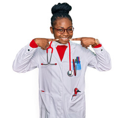 Young african american woman wearing doctor uniform and stethoscope smiling cheerful showing and pointing with fingers teeth and mouth. dental health concept.