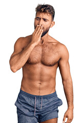 Fototapeta premium Young hispanic man wearing swimwear shirtless bored yawning tired covering mouth with hand. restless and sleepiness.