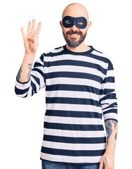 Naklejka premium Young handsome man wearing burglar mask showing and pointing up with fingers number four while smiling confident and happy.