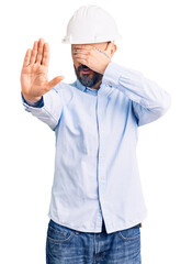 Young handsome man wearing architect hardhat covering eyes with hands and doing stop gesture with sad and fear expression. embarrassed and negative concept.