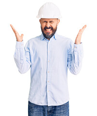 Young handsome man wearing architect hardhat celebrating mad and crazy for success with arms raised and closed eyes screaming excited. winner concept