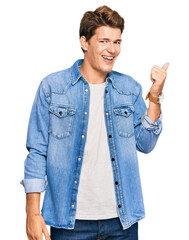 Handsome caucasian man wearing casual denim jacket smiling with happy face looking and pointing to the side with thumb up.