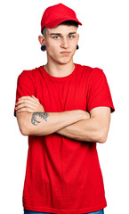Young caucasian boy with ears dilation wearing delivery uniform and cap skeptic and nervous, disapproving expression on face with crossed arms. negative person.